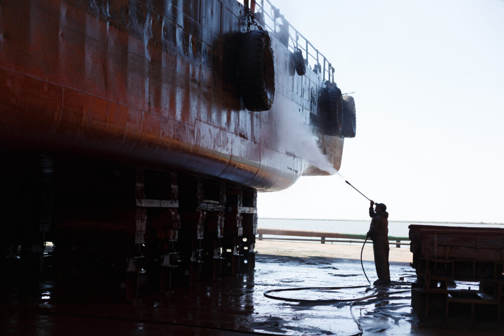 A person cleaning a vessel with a pressure washer.