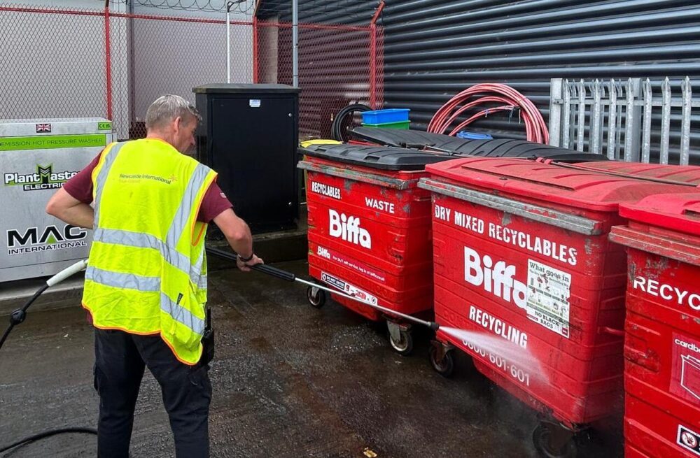 A worker using the MAC Plantmaster pressure washer to clean bins outside.